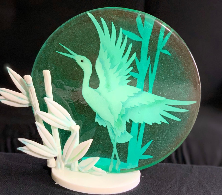 A sugar art night light features a glowing green heron in flight against a circular translucent sugar backdrop, accompanied by a 3D white sugar bamboo sculpture on a cream-colored base.