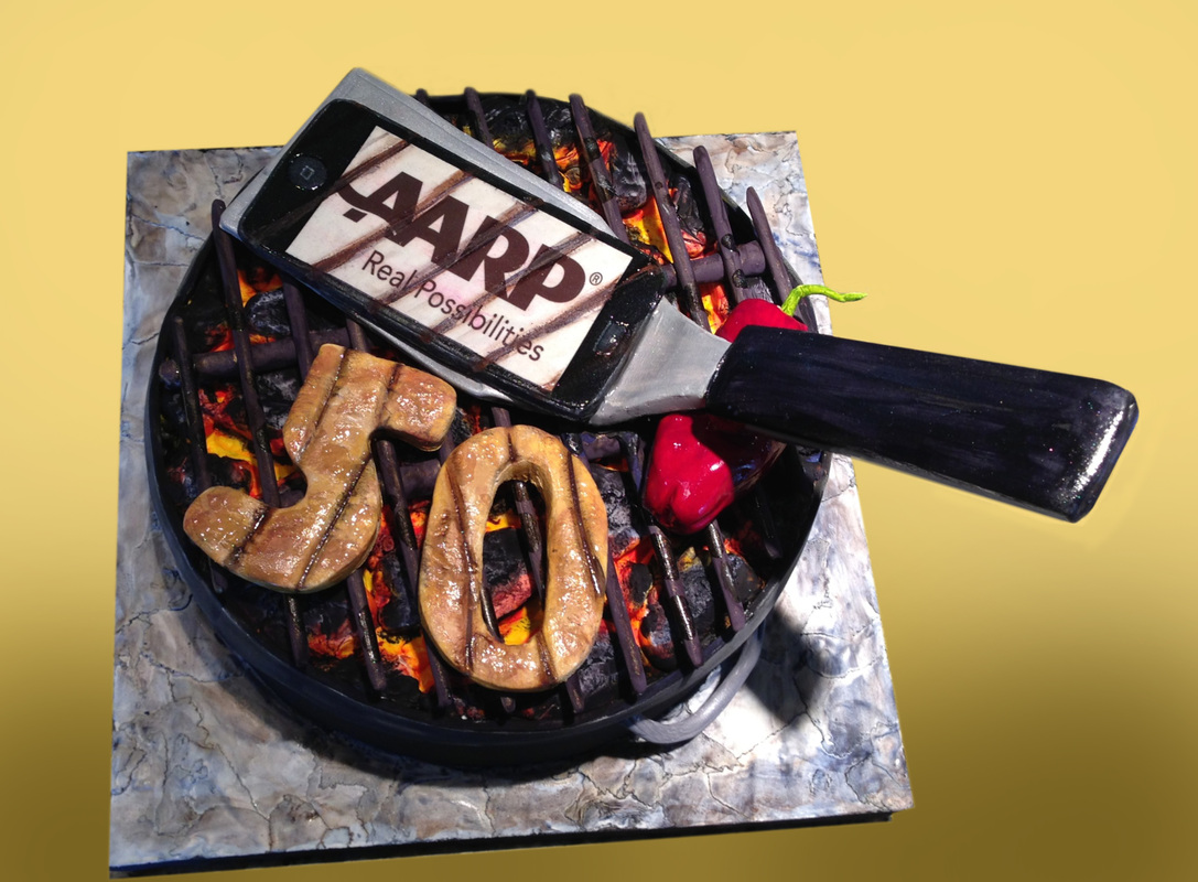A hyper-realistic cake designed to look like a charcoal grill features grilled numbers spelling "50," a red pepper, and a spatula lifting a smartphone displaying the AARP logo.