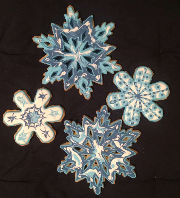 Four intricately decorated snowflake-shaped cookies featuring blue and white icing designs are arranged on a black background.