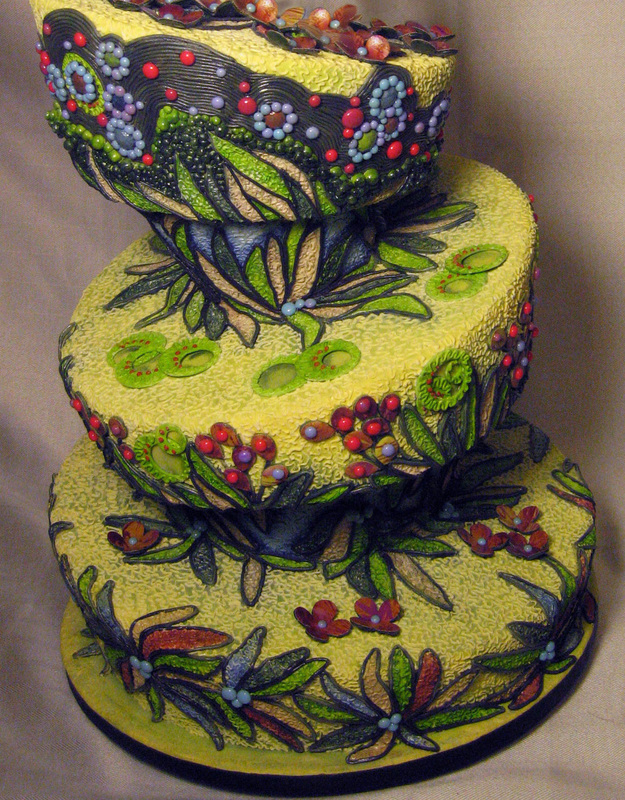A three-tiered yellow cake features intricate, hand-painted botanical designs with green leaves, red berries, and colorful flowers on each level.