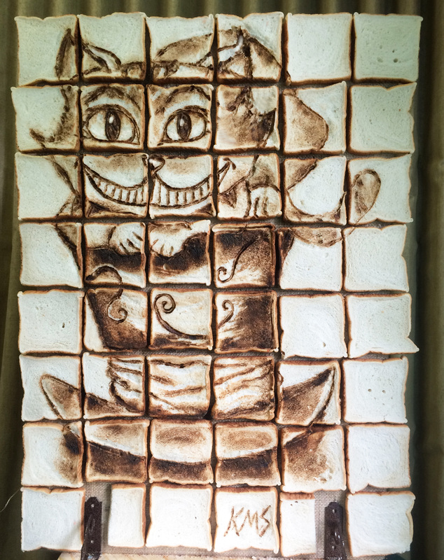 Toasted marshmallows arranged in a pixelated grid form a mosaic portrait of the Cheshire Cat, featuring its signature wide grin and striped body, with the initials "KMS" branded into the bottom center square.