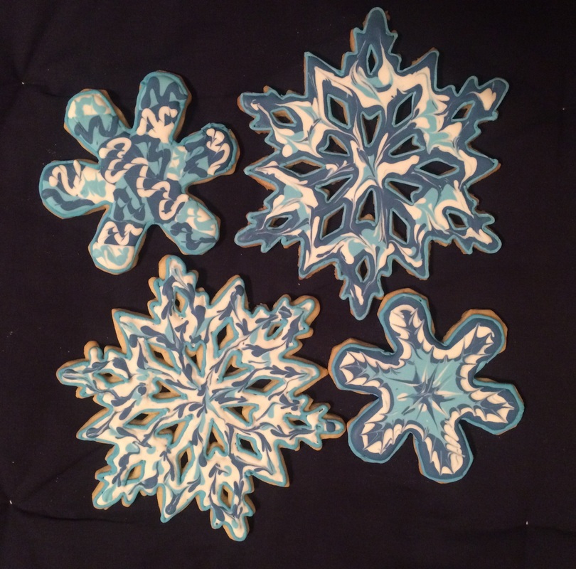 Four intricately decorated snowflake-shaped cookies with blue and white marbled icing are arranged on a dark background.