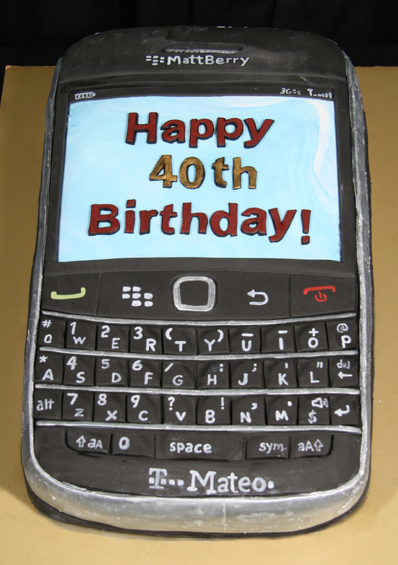 A detailed cake sculpted to resemble a black BlackBerry smartphone, featuring a light blue screen with "Happy 40th Birthday!" written in red and gold icing, along with realistic keyboard buttons and branding details.