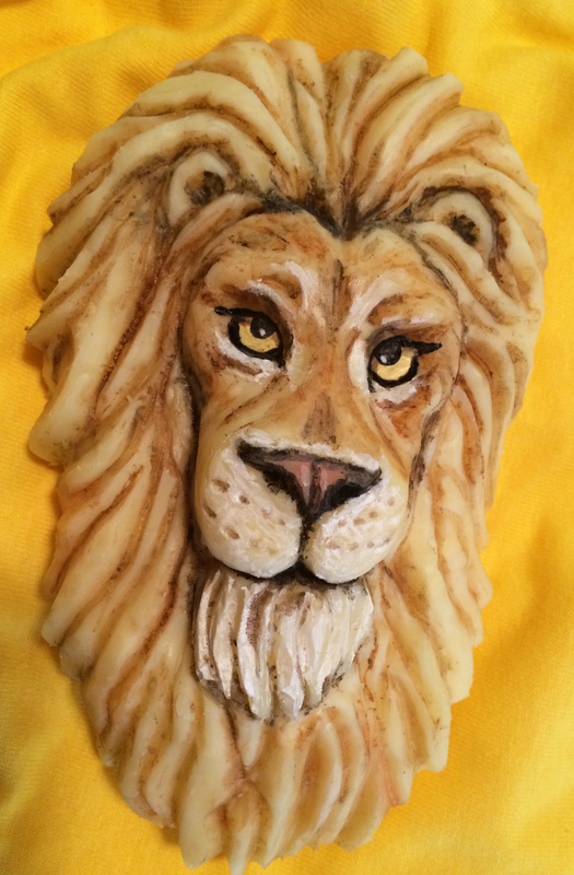 A sculpted lion head with detailed facial features and textured mane rests against a bright yellow fabric background.