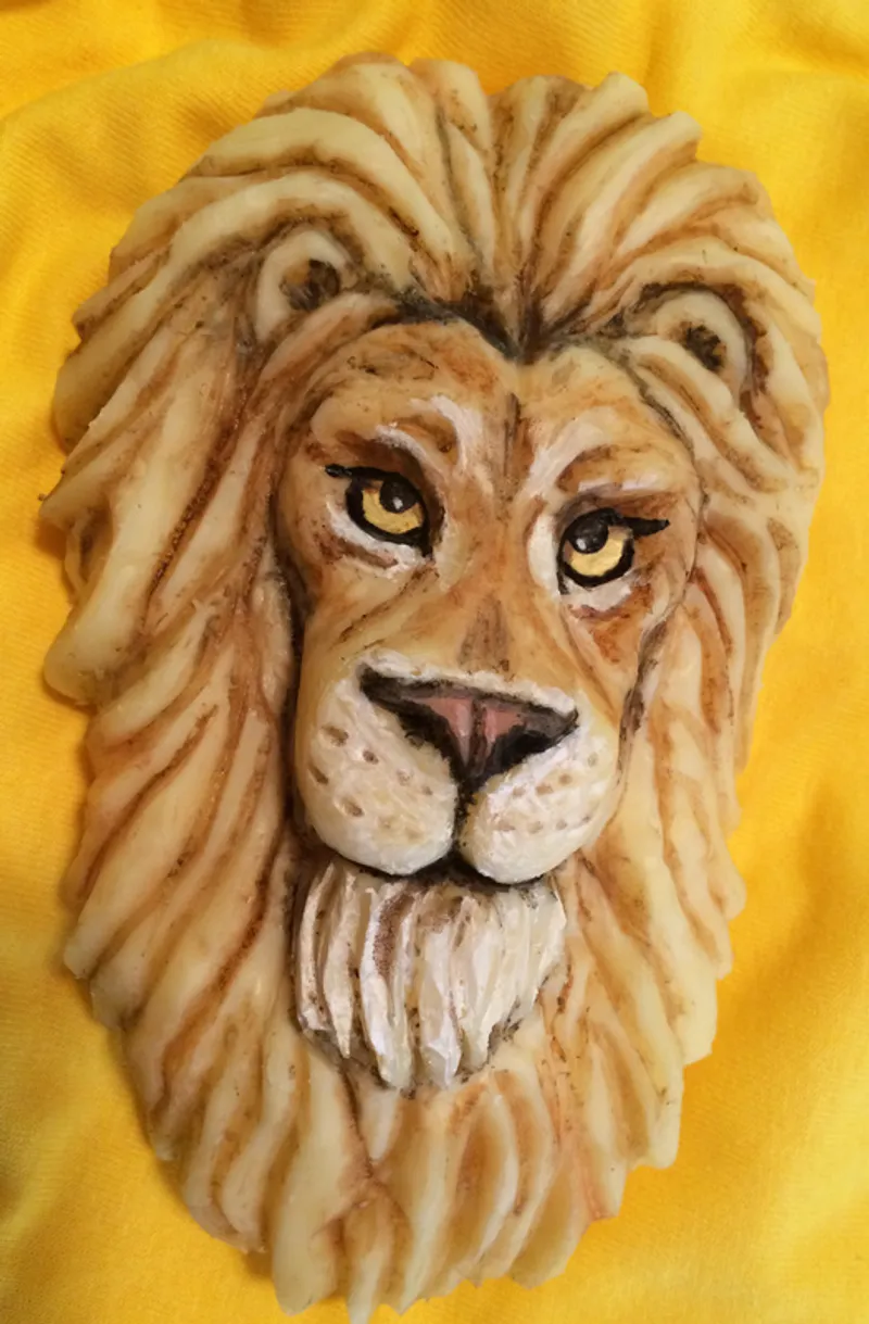 A sculpted lion head with detailed facial features and textured mane rests against a bright yellow fabric background.