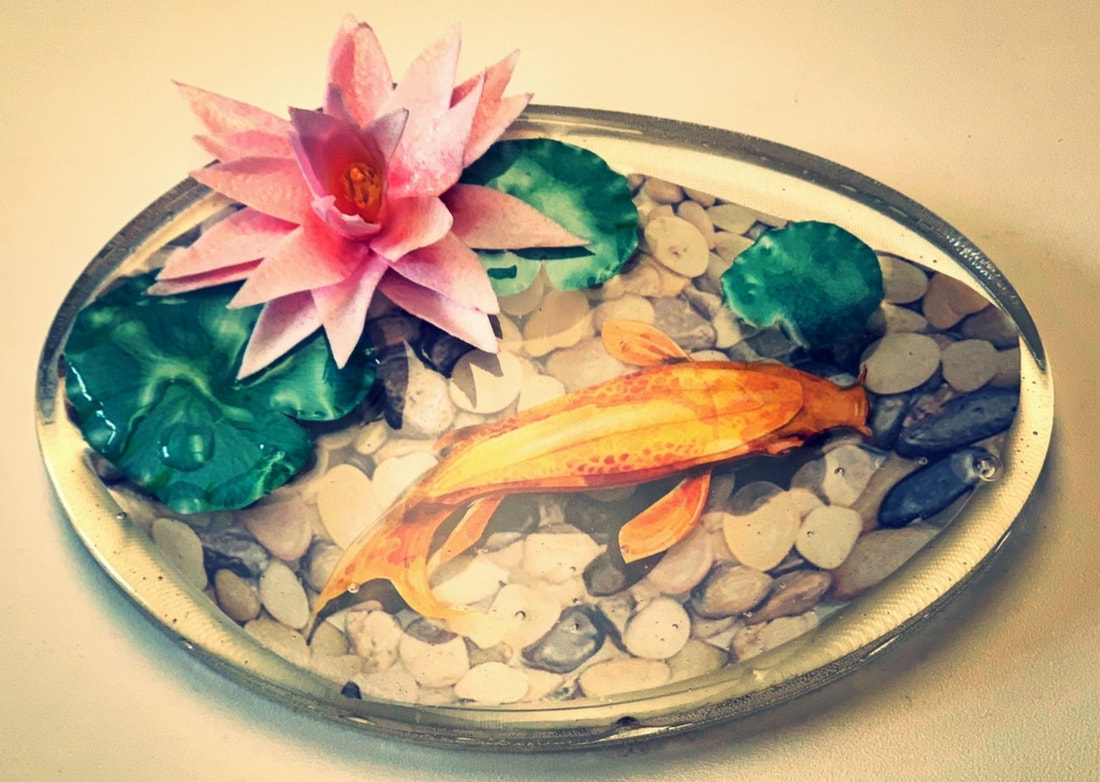 A sugar art glass-like tray features an edible printed design of a koi fish swimming among pebbles, lily pads, and a pink water lily.