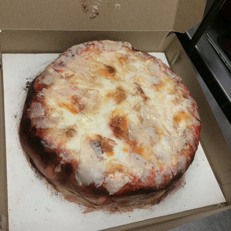 A cheese pizza with a thick, dark crust sits in an open cardboard box on a white paper liner.