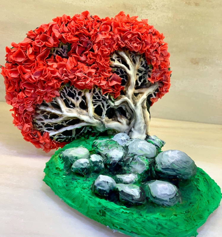 A sculpted sugar bonsai-style tree with a white, gnarled trunk and vibrant red, textured foliage sits atop a bright green base adorned with smooth, grey sugar stones.