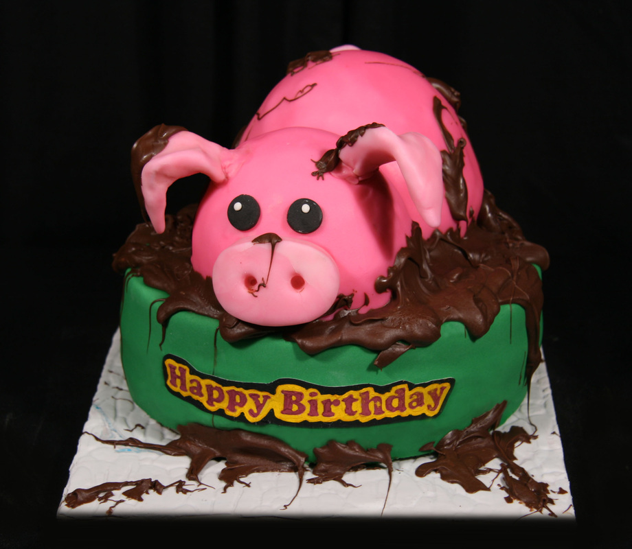 A pink pig-shaped birthday cake sits in a green mud puddle decorated with chocolate icing and a "Happy Birthday" banner.