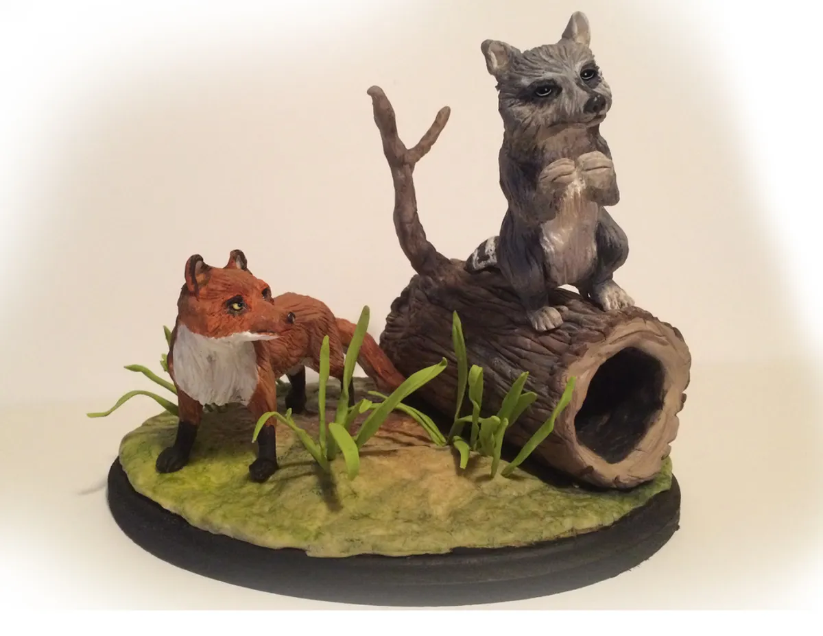 Hand-painted mini diorama of a red fox and raccoon beside a hollow log.
