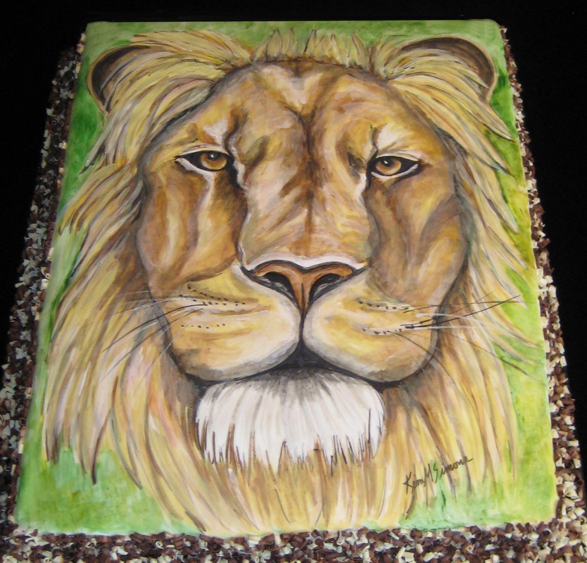 A realistic sculpted cake featuring a male lion's head with a golden mane and white beard, set against a green background and signed by the artist in the bottom right corner.