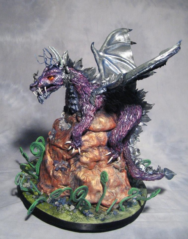 A detailed miniature figurine of a purple dragon with metallic silver wings perched atop a rocky base surrounded by green vines.