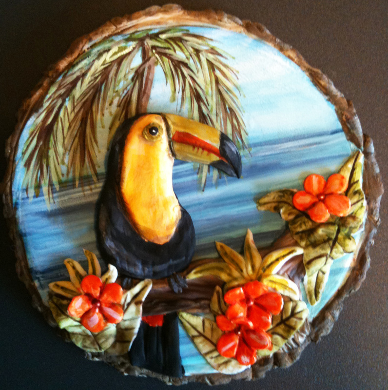 A sculpted cake in the shape of a toucan perched among vibrant orange flowers and palm fronds, displayed on a rustic wood slice base against a blue sky backdrop.