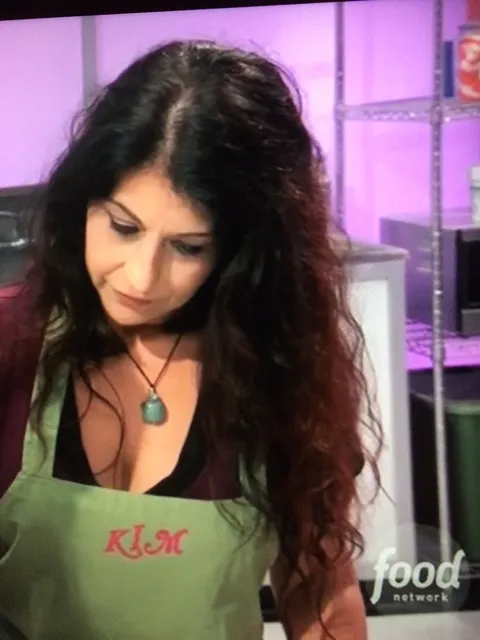 Kim Simons in a green apron with the Food Network logo in the background.