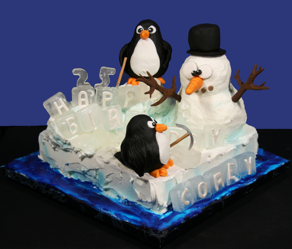 A rectangular birthday cake decorated with a winter theme features a snowman wearing a top hat, two penguins, and translucent ice cube-shaped letters spelling "HAPPY BIRTHDAY COREY 25" on a blue marbled base.