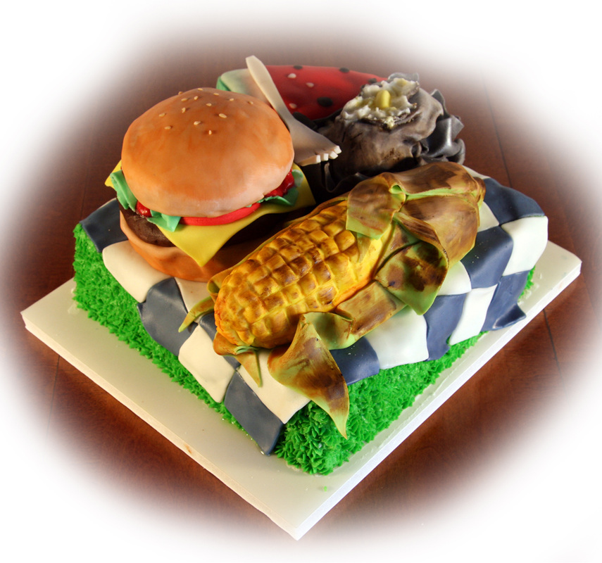A square cake decorated to resemble a picnic scene features a realistic hamburger, an ear of corn, a watermelon slice, and a dessert on a blue and white checkered blanket atop green grass.