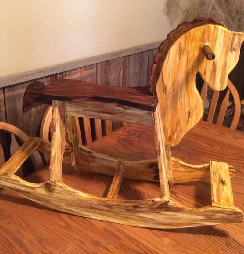 A sculpted sugar rustic wooden rocking horse with a live-edge seat and natural wood grain sits on a dining table.