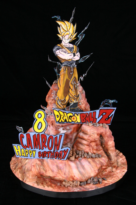 A Dragon Ball Z themed birthday cake features a sculpted figure of Super Saiyan Goku standing atop a rocky base, surrounded by edible signs reading "8," "Dragon Ball Z," and "Camron Happy Birthday."