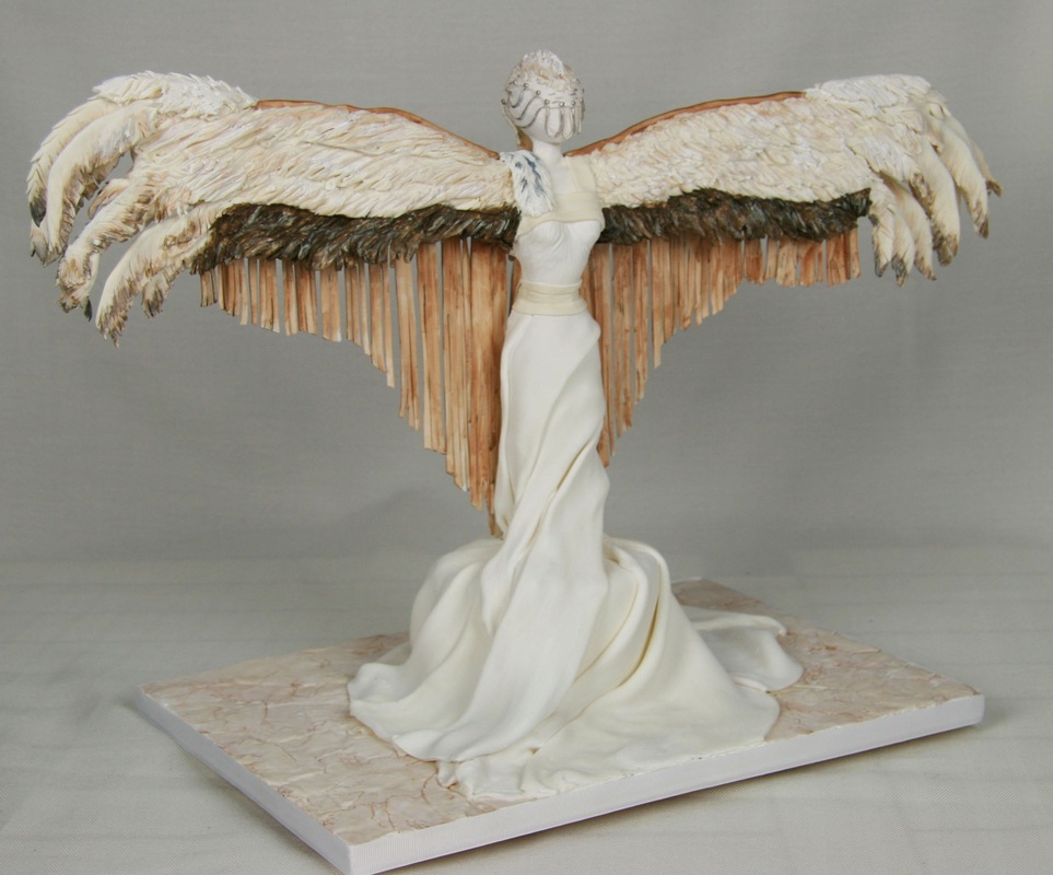 A white sculptural figure of a winged woman in a flowing gown stands on a marble-like base, featuring large, textured wings with layered feathers and a face composed of vertical white elements.