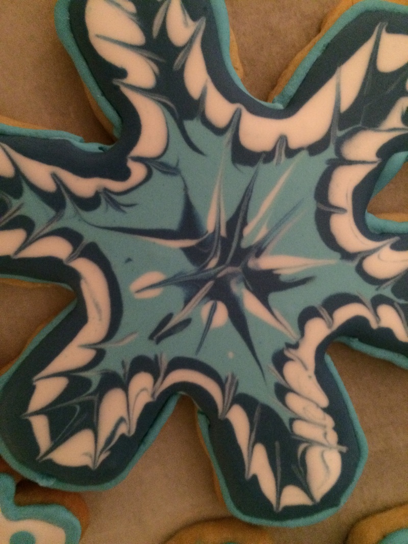 A close-up of a star-shaped sugar cookie decorated with teal, black, and white icing in a symmetrical, feathered pattern.