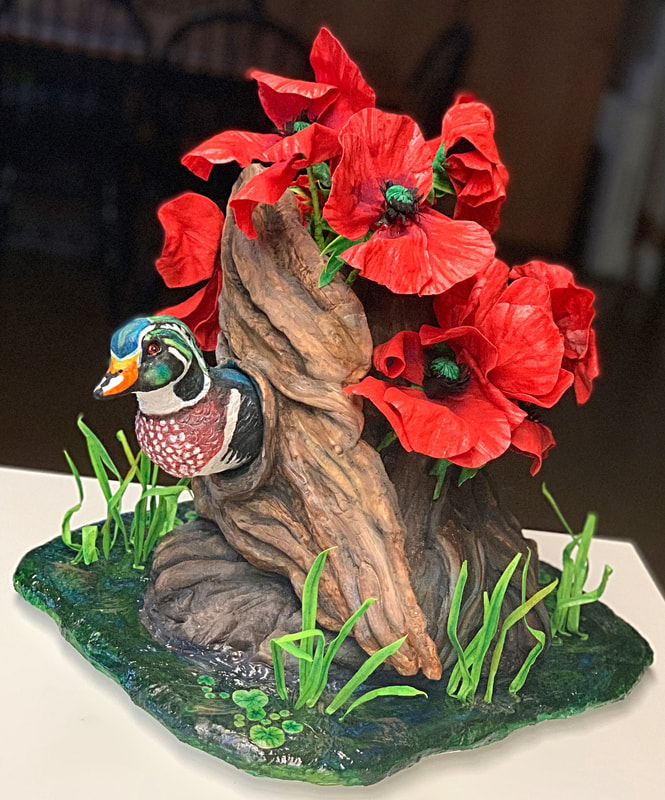 A detailed figurine depicts a colorful wood duck perched beside a gnarled tree stump adorned with vibrant red poppies and green grass.
