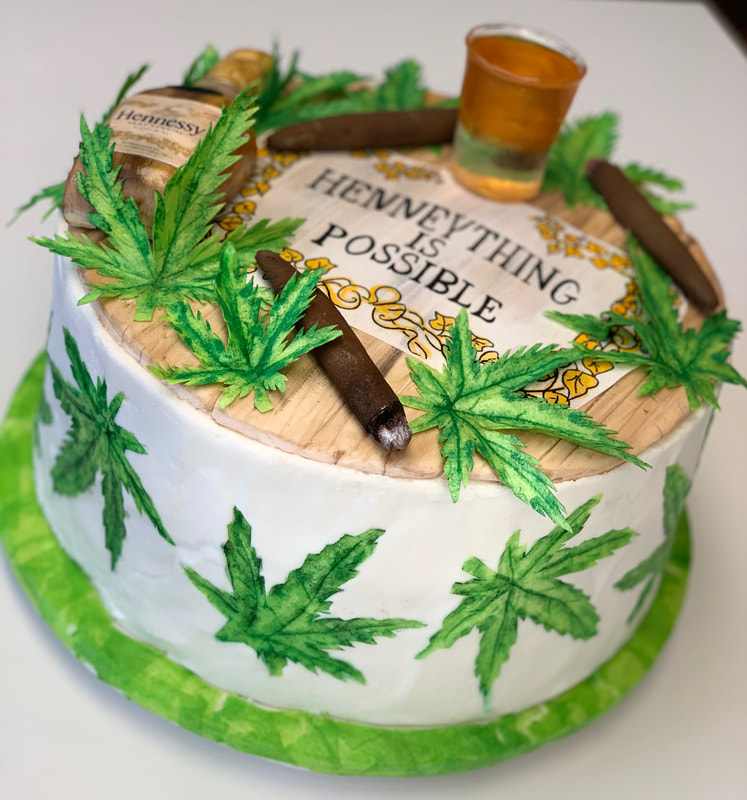 A white frosted cake decorated with green cannabis leaves features a top design resembling a wooden barrel lid, adorned with fondant cigars, a Hennessy bottle, a shot glass, and the text "Henneything Is Possible."