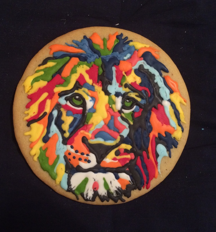 A round sugar cookie decorated with colorful icing in shades of blue, orange, yellow, green, and red, forming a vibrant, abstract lion's face with black outlines and white accents.