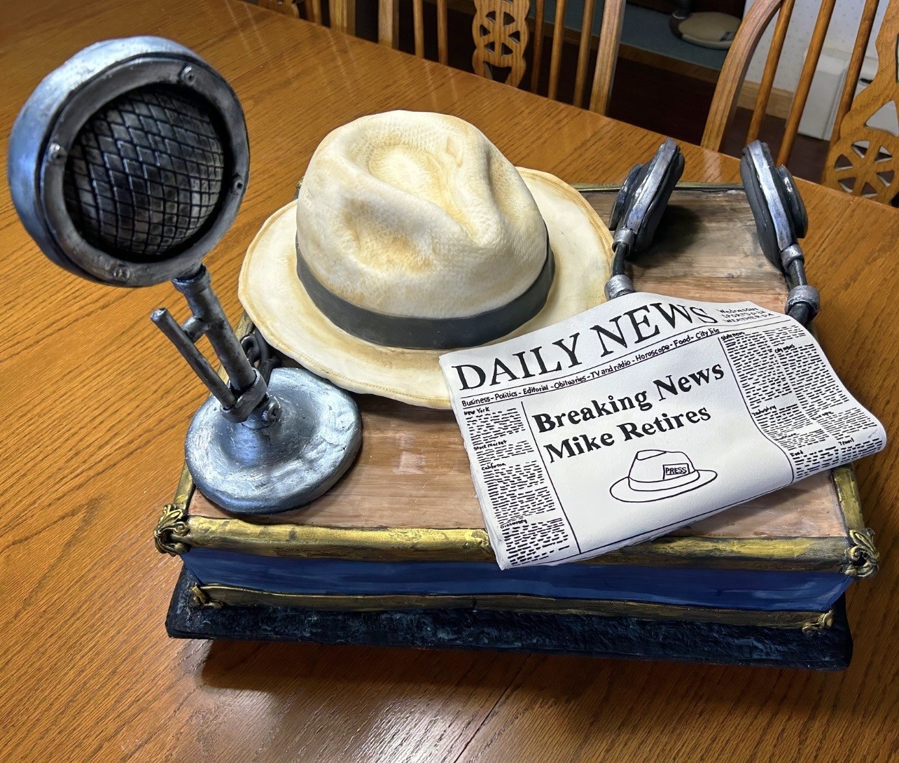 A 90th birthday sculpted cake shaped like a rugged mountain peak with white and light blue snow-capped frosting, lower section transitioning to lush green grass with handcrafted fondant flowers, large "90" topper made from printed medical diagrams, miniature red mountain bike on snowy slope, red skis in snow, tiny fondant hiking boots, backpack, and golf club at base.