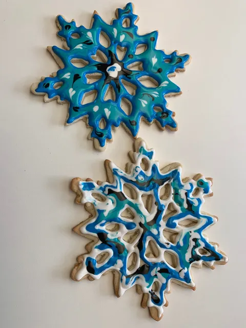 Two sugar cookies decorated with marbled blue, white, and black snowflake designs
