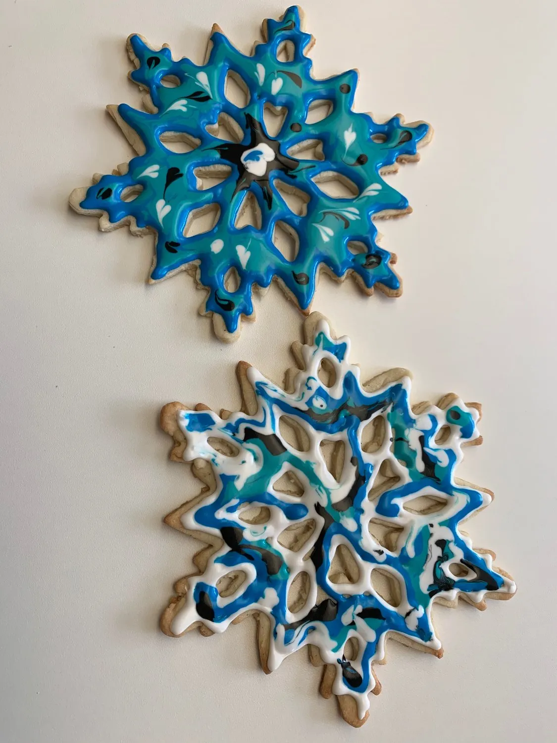 Two sugar cookies decorated with marbled blue, white, and black snowflake designs