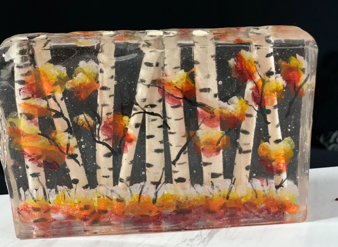 A rectangular block of clear sugar glass encapsulates a painted autumn scene featuring white birch trees with black markings, surrounded by vibrant red, orange, and yellow sugar foliage against a dark background.