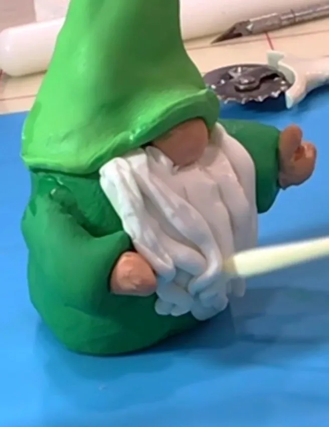 White fondant beard strips being added to the gnome figure.