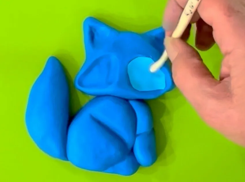 Hand using a cake tool to add lighter fondant detail to the chest.