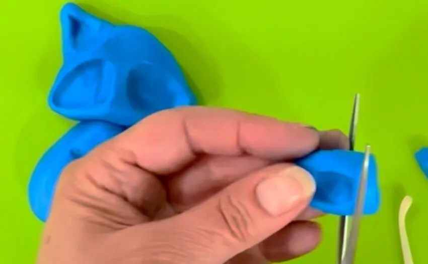 Hand cutting blue fondant with scissors to shape the ears.