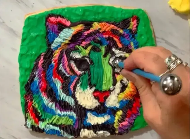 Hand using a ball tool to indent eye sockets on the tiger cookie.