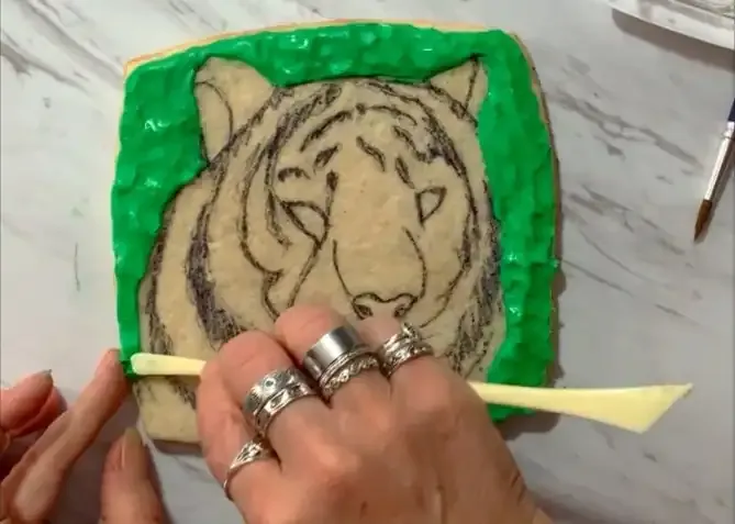 Hand piping green modeling chocolate around the tiger sketched cookie.