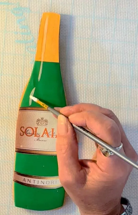 Hand using a fine brush to add white petal dust highlights to the bottle cookie.