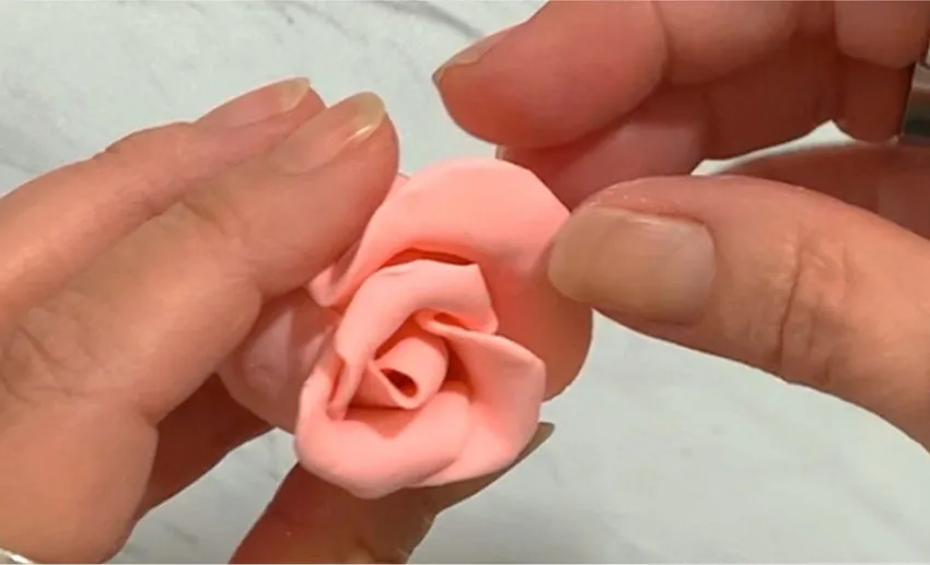 Hand adding layered modeling chocolate petals to the rose.