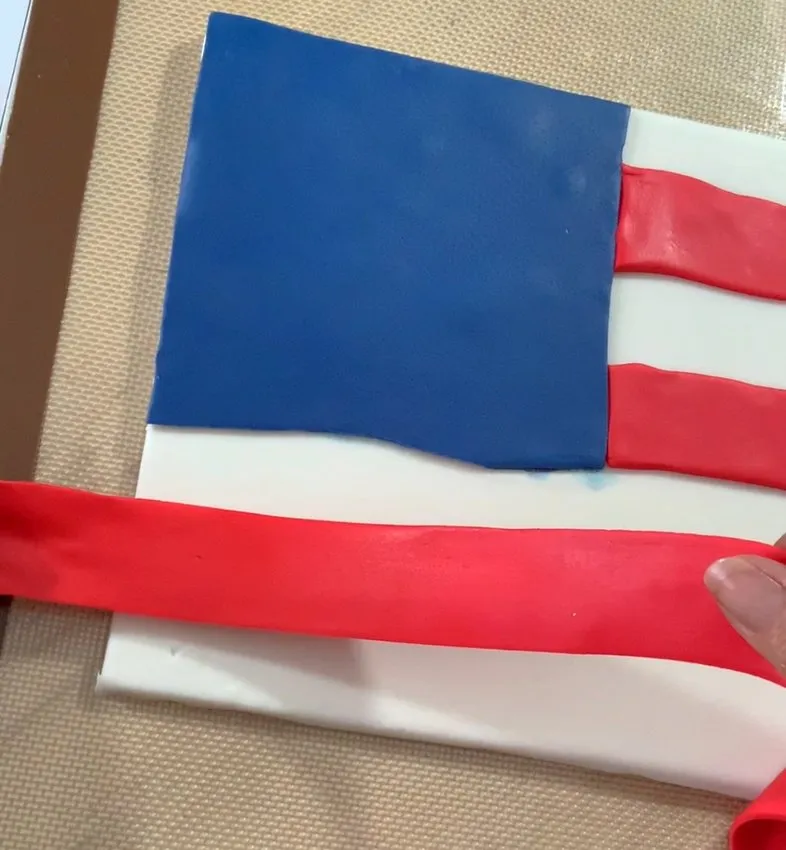 Hand placing a red fondant stripe onto the American flag cake.