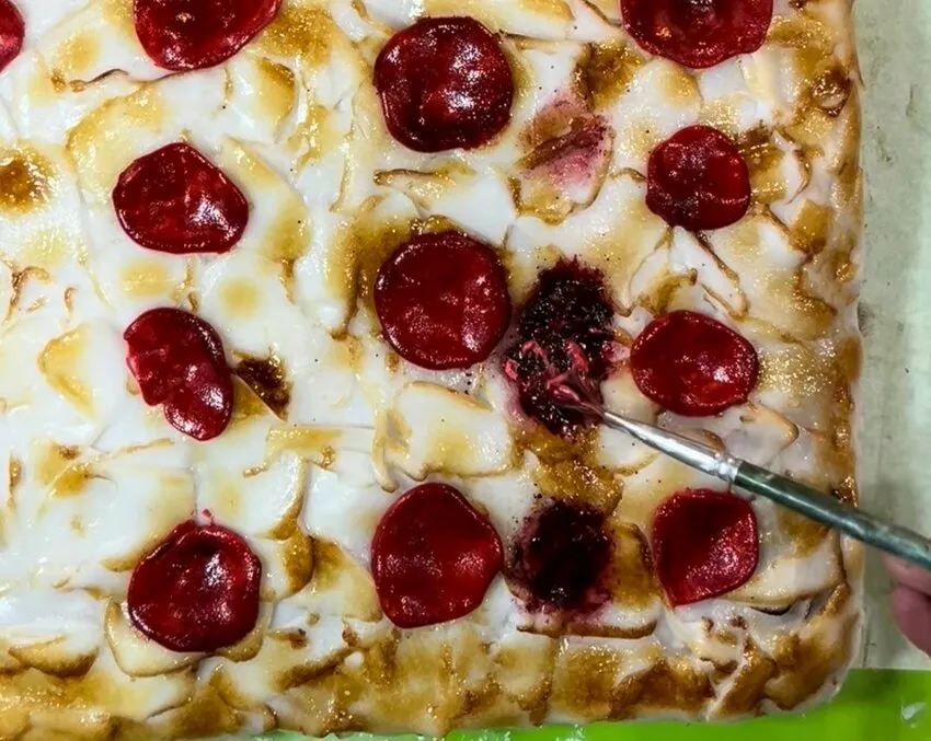 Applying red buttercream sauce to the pizza cake.