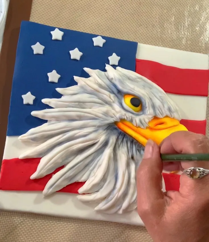 Hand adding shadows and highlights with edible colors to the eagle.