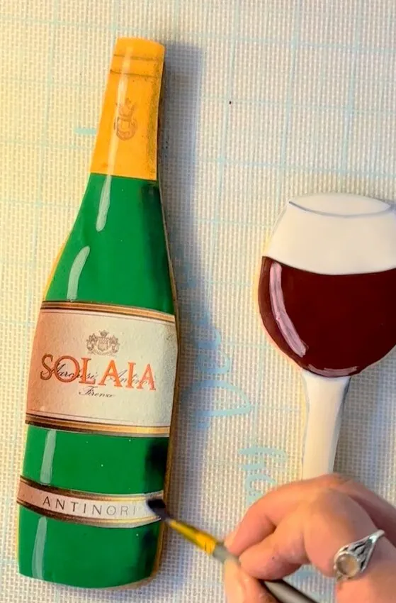 Hand adding shadow details with petal dust to the bottle and glass cookies.