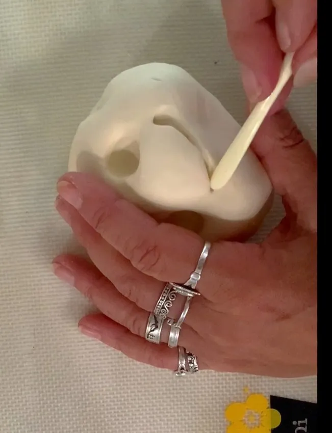 Hand using a cake tool to carve a smile on the fondant bunny face.