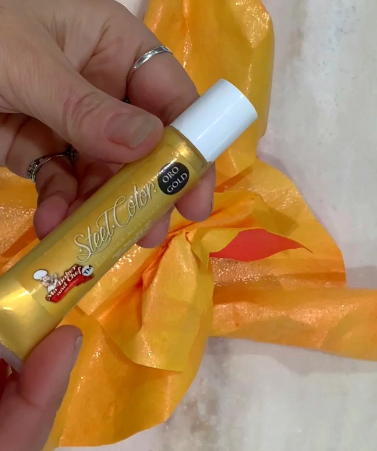 Hand holding a tube of gold jewel color over wafer paper petals.