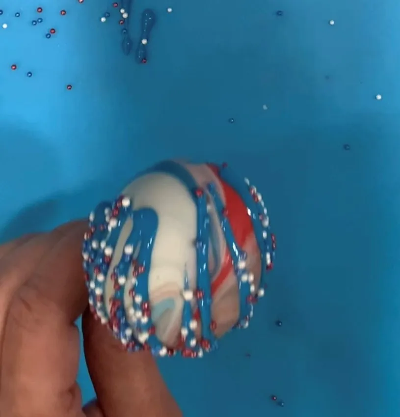 Cake pop decorated with patriotic sprinkles on a colored background.