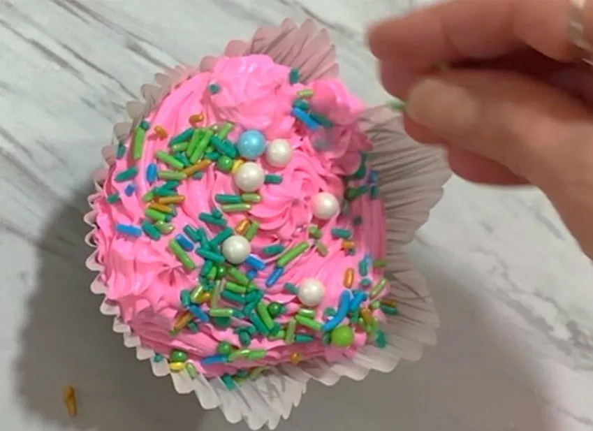 Cupcake with pink buttercream topped with colorful sprinkles.