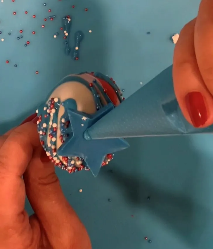 Hand adding a chocolate star decoration to a finished cake pop.