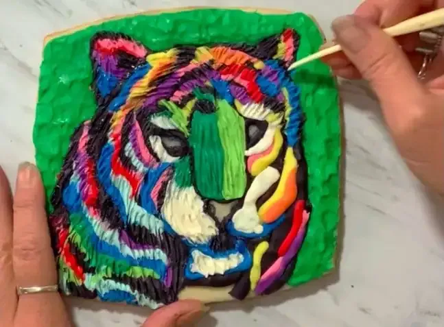 Hand using a clay tool to add fur texture to the modeling chocolate tiger.