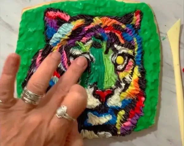 Hand adjusting yellow modeling chocolate eyes on the tiger face.