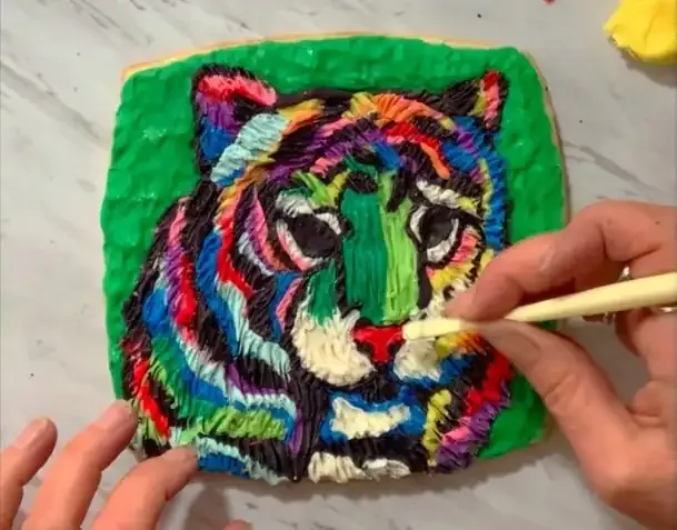 Hand adding modeling chocolate nose details to the tiger cookie.